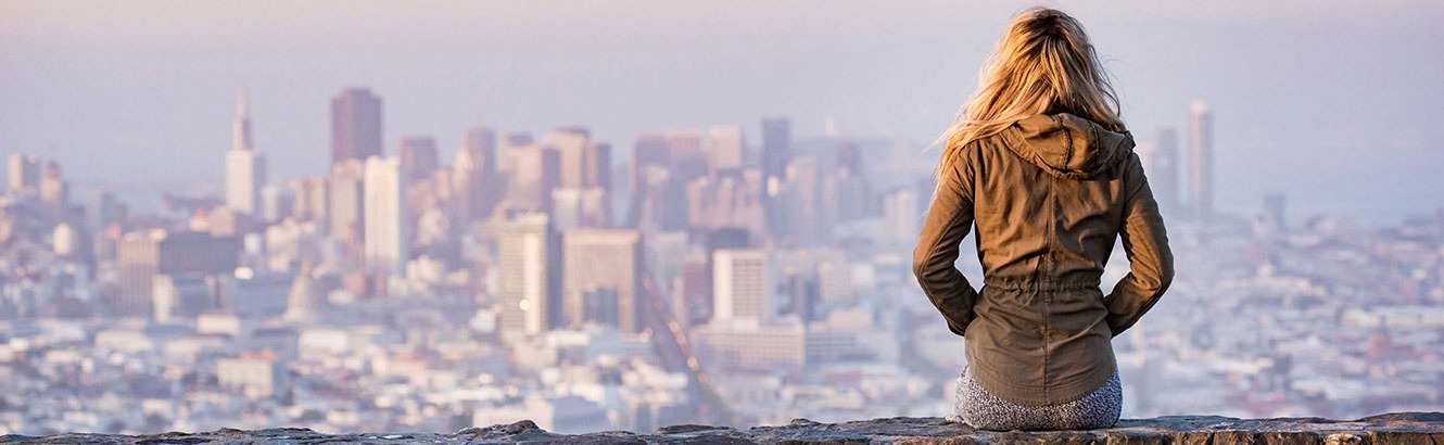 Long haired woman in a leather coat looking out over a city