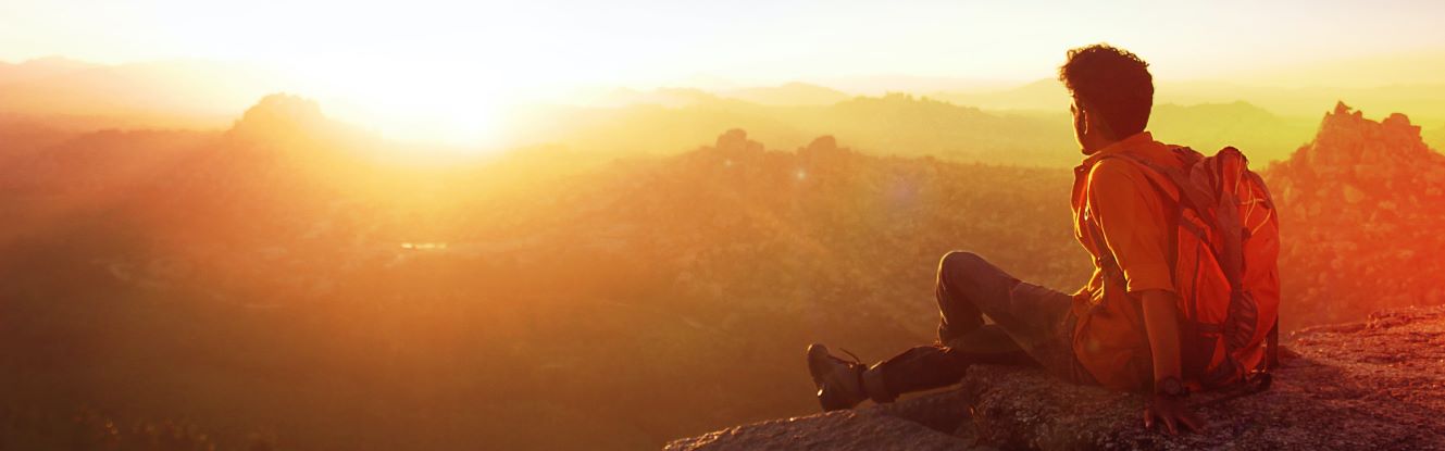 Man sitting on a mountain ridge watching a sunset.